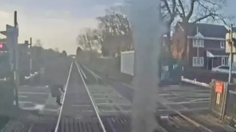 Woman steps out and then can be seen tilting back off the tracks as a train comes