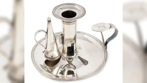 Woolley & Wallis A silver chamberstick and snuffer, with a plate at the bottom. It is against a white background.