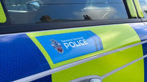 A picture of the side of the Devon and Cornwall police vehicle. It is green and blue in colour and has the forces blue logo on the side. 