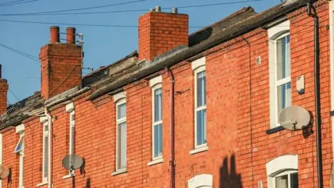 A row of red brick terraced houses can be seen, some with satellite dishes. 