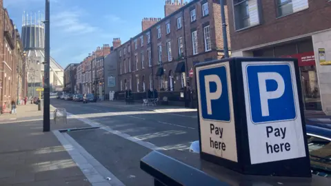 Blue parking sign which says "pay here" by Hope Street, with old Georgian houses on both sides and Liverpool's Metropolitan Cathedral in the background.