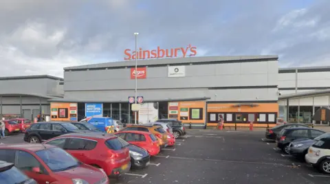 Google Streetview The outside of a large Sainbury's supermarket entrance with a full car park