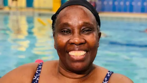 Lucy Kabui wearing a black swim cap and smiling at the camera from the swimming pool.