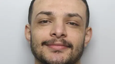 National Crime Agency Custody picture of a man with a short beard smiling.