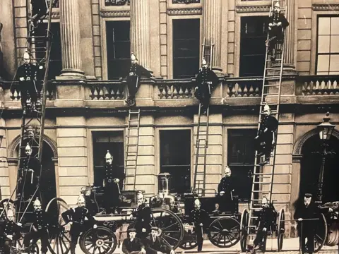 Museum of Scottish Fire Heritage An archive photo of Inverness fire brigade shows about a dozen firefighters posing for the camera in from of a large stone building. The firefighters are standing on or around an old fire appliance. Four of the firefighters are posing leaning half way up ladders propped up against the building