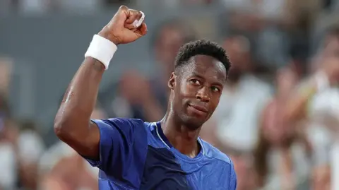 Gael Monfils, wearing a blue t-shirt, looks up to his right and raises his right fist