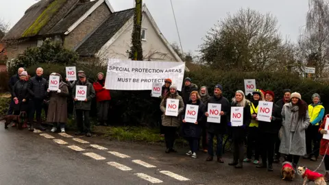Joao Santos/LDRS A large group of protesters – made up of men and women – on a village road. They are holding up signs which read "Say NO to Cranswick" and a large banner which reads "Special Protection Areas Must Be Protected".