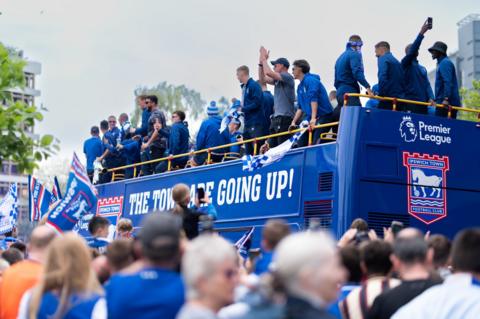 Ipswich Town players celebrate on an open-top bus above a crowd