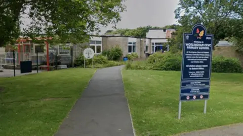 Google Maps A photo showing the entrance to a one-storey primary school building. It is set amongst a few trees. On the right of the image is a navy blue sign which says Welcome to Worlingham CEVC Primary School on it.