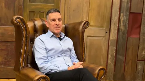 The author wearing a pale blue shirt sitting in a high-backed leather armchair.