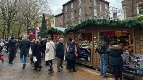 York christmas market with wooden chalet stalls and a number of people shopping. 