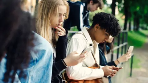 Stock photo shows teens outside looking at phones