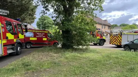 Suffolk Fire and Rescue Service Four fire service vehicles parked in front of a house and behind a tree.