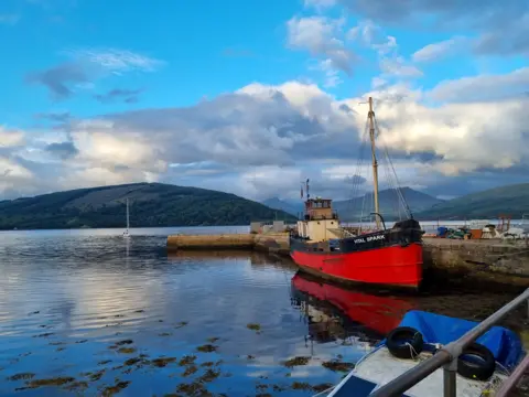 Jennifer Mills A small red and white boat sits at a pier with hills in the background
