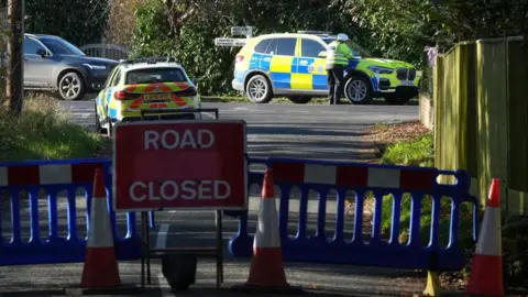 Eddie Mitchell A road closed sign with two police cars and a police officer in the background.