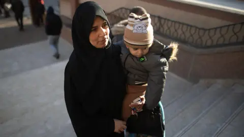 EPA-EFE/Rex/Shutterstock is a Palestinian woman wearing a child with a child with a black beany, moving up the stairs. 