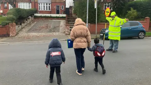 Lollipop man Barry Jones helping a family cross the road in Heywood