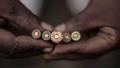 A close up of a pair of hands holding five bullets.