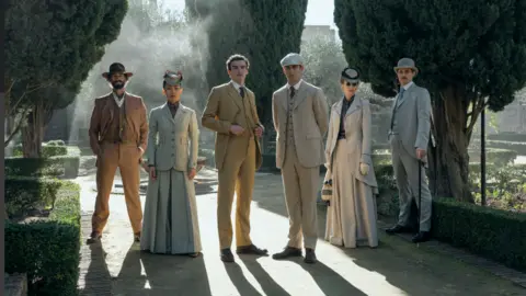 Daniel Smith/ Amazon MGM Studios Set in a garden, four men and two women stand looking at the camera. All dressed in 19th century period clothing. The men in three piece suits, and the women in tailored jackets and skirts.