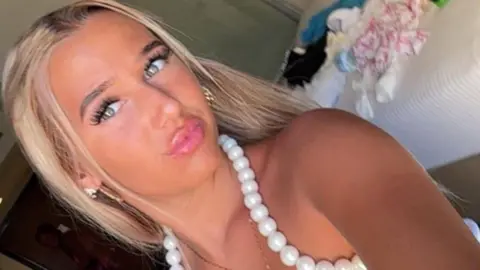 Chloe Watson Dransfield is pictured looking directly at the camera and pouting. She has long, blonde hair and is wearing a white top with beading around the neck line.