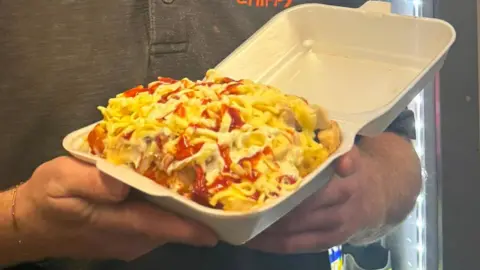 A chick box in a plastic container held up with two hands. It is covered in suace.