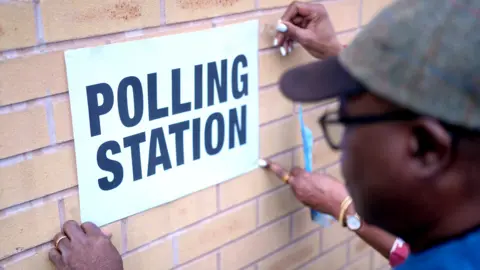 Staff put up signs outside the polling station at St Agnes Primary School on February 26, 2026 in Manchester, England. 