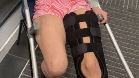 Jessica Gatherer Jessica Gatherer wearing a knee brace. She is sitting on a chair holding crutches.