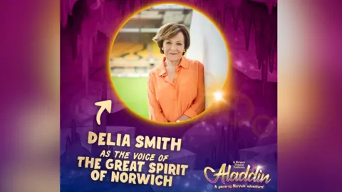 Norwich Theatre Royal A promotional poster featuring Delia Smith. She is wearing an orange shirt while standing at Carrow Road stadium, an the poster advertising her performance in a pantomime is in purple and pink.