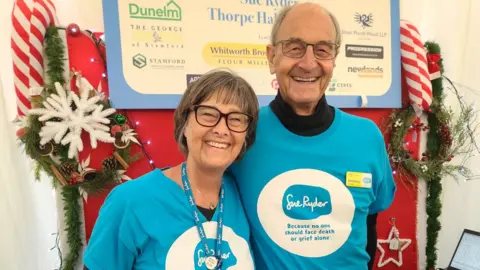 Sue Ryder A man and woman smile with their arms round each other. They are both wearing blue T-shirts with "Sue Ryder" written on them.