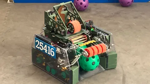 A small green and orange robot with 26416 written on the side of it in white numbers.