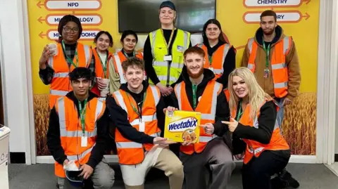 Weetabix Nine of the young people from the project in a group photo wearing hi-vis waistcoats and lanyards holding a box of Weetabix, with a female member of Weetabix staff.