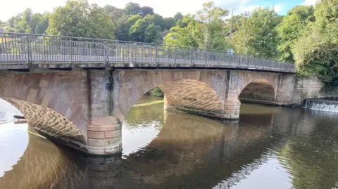 This shows a bridge over the River Derwent at Belper. It's a stone bridge and designed with three arch shapes. The bridge allows vehicles and pedestrians to cross the river. 