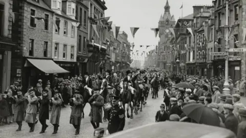 Getty Images A black and white picture of Hawick common riding heading along the main street with a band leading a huge cavalcade with big crowds on both sides of the street
