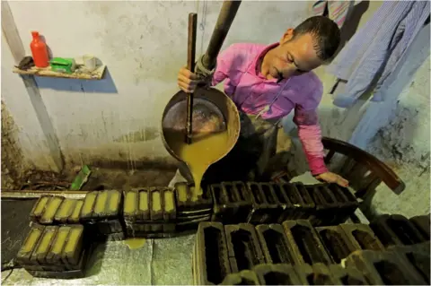 Getty Images A man pouring yellow liquid into rectangular containers.