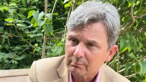 Man with grey hair wearing beige suit