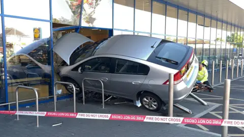 A silver car with its bonnet through the front of a Lidl window.