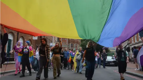 Pride Pictures & Kerry Kleis photography Festival goes walking the streets of Reading holding an LGBT flag of rainbow colours above their heads.