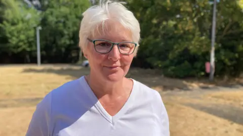 A woman with white hair, glasses and a white top looks at the camera.