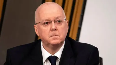 Getty Images Peter Murrell - a bald man with glasses, wearing a dark suit and tie - pictured looking solemn during a Scottish Parliament committee meeting in 2021