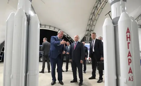 Getty Images Russian President Vladimir Putin (C) listens to Dmitry Rogozin (L), head of Russia's space agency Roscosmos, as they visit the Vostochny cosmodrome, Amur region, on September 4, 2021
