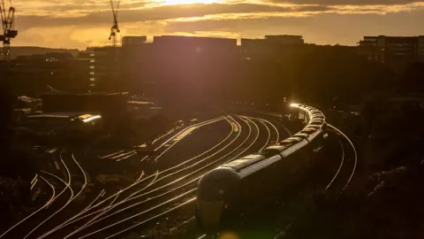 Getty Images A Great Western Railway train approaches Bristol Temple Meads Station. The picture is taken at sunset with the tracks glowing bright in the setting sun and the sky tinged with orange. Buildings and cranes are silhouetted in the background