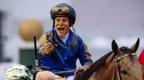 Reuters Covered in mud, Jockey Junior Alvarado celebrates atop Derby winner Sovereignty, a brown horse.