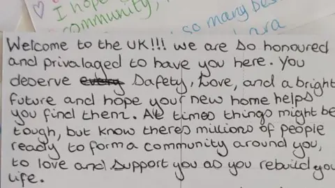 CONVERSATIONS OVER BORDERS A note with a handwritten message that reads Welcome to the UK! We are so honoured to have you here. You deserve safety, love, and a bright future and hope your new home helps you find them. At times things might be tough, but know there's millions of people ready to form a community around you, to love and support you as you rebuild your life.