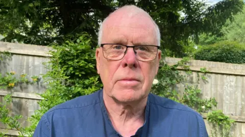 John Podmore John Podmore is standing in front of a fence in a garden