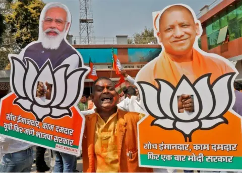 AFP Supporter of India"s ruling party Bharatiya Janata Party (BJP) displays cut-outs of Prime Minister Narendra Modi and Chief Minister of Uttar Pradesh Yogi Adityanath as he celebrates after learning the initial poll results outside its party office in Lucknow, India, March 10, 2022