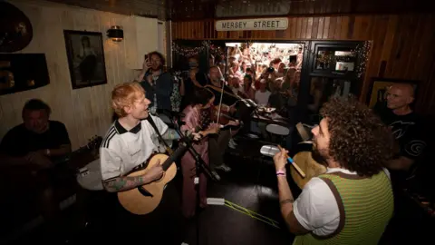 Mark Surridge Ed Sheeran singing and playing a guitar in a pub. 