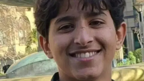 Abdullah looks into the camera with a smile showing his teeth. He has short dark hair.