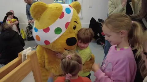 BBC Children In Need Pudsey the bear hugging two children at the charity centre