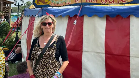 Woman wearing sunglasses and red bow in her hair smiles at the camera in front of a white, red and blue tent with wooden flag pole to the left