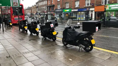 Motorcyles parked on pavement on Epsom high street, shops, including KFC and Subway, in the background.